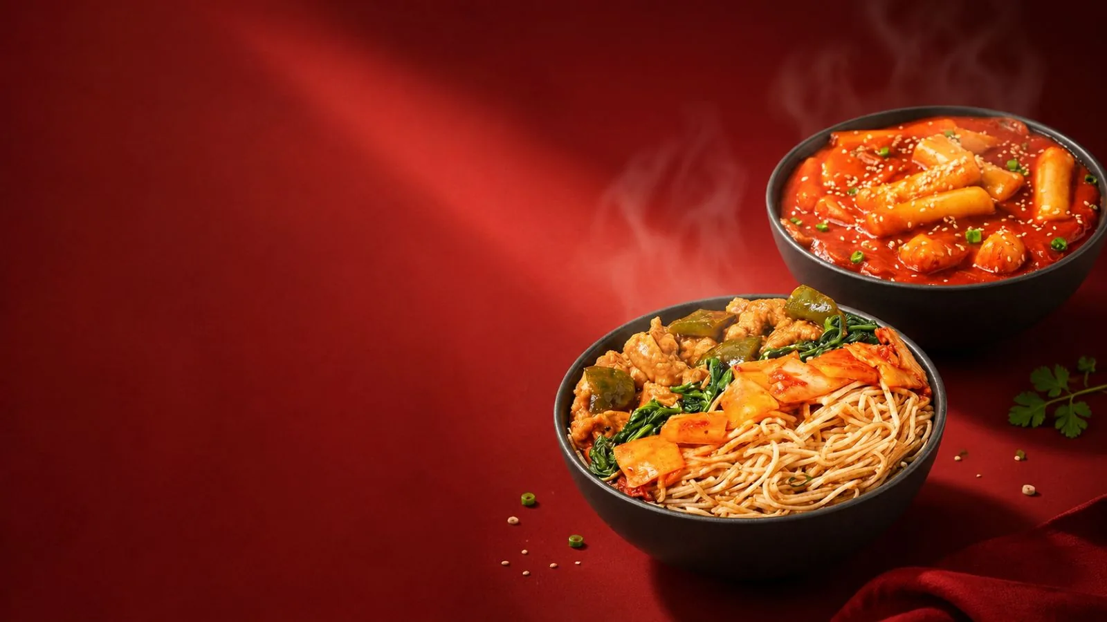 Steaming bowls of Korean topokki and stir-fried noodles on a bold red backdrop